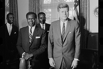 John F. Kennedy standing in the Oval Office with several prominent Black individuals.