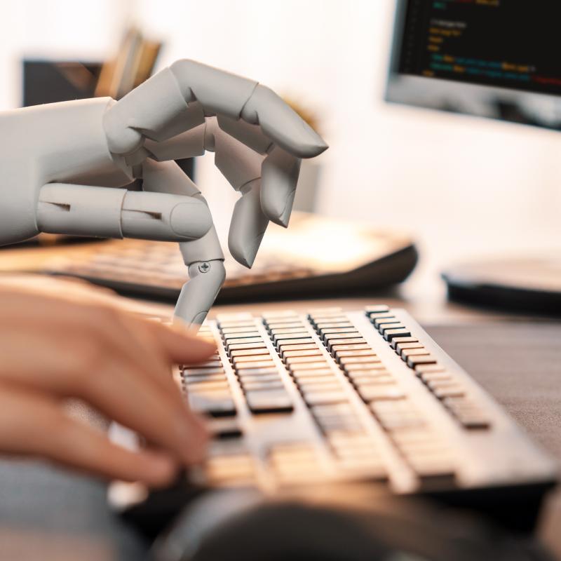 human hand and robotic hand typing on computer keyboard