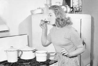 A black and white picture from the 1950s to early 60s showing a wife in the kitchen